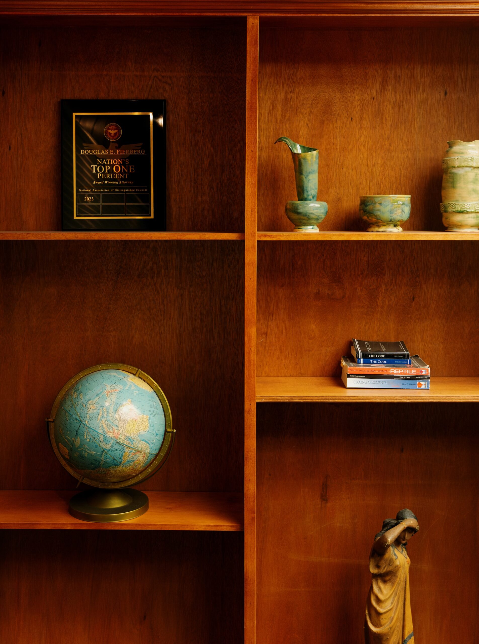 Douglas E. Fierberg's wooden office bookshelf displays his Top One Percent Solicitor award, a globe, law books, and green pottery.